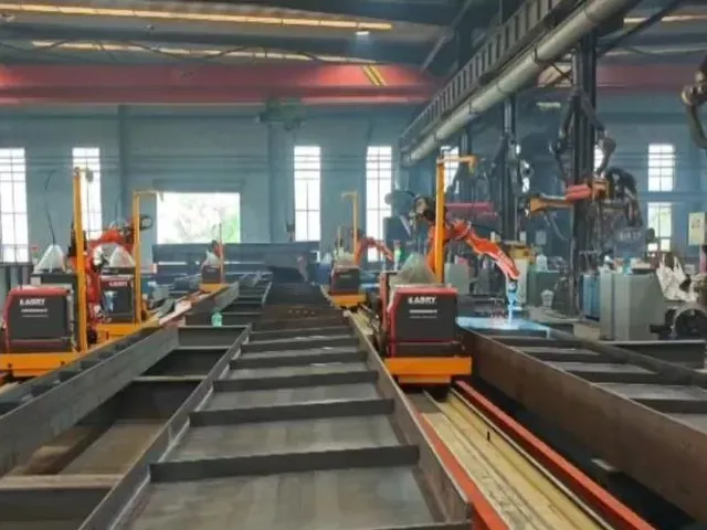 Rail-mounted welding robots beside a wide crane runway beam with transverse stiffeners.
