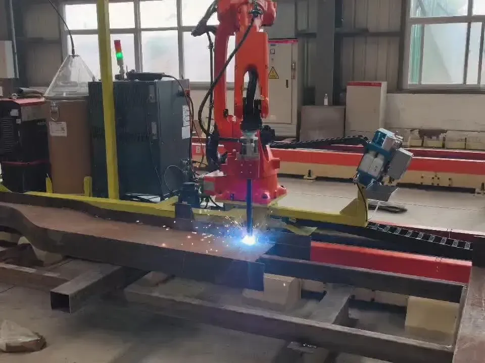 Robot soudant un élément en acier avec âme et semelle courbes, avec des étincelles à la torche.
