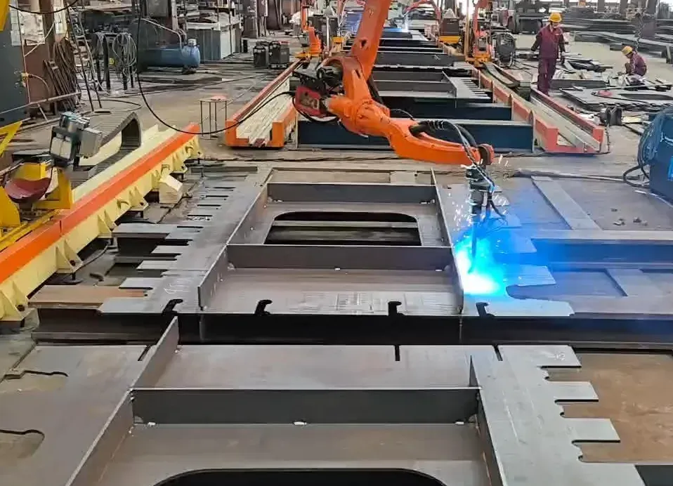 Robot orange soudant un grand assemblage de tôles avec ouvertures et raidisseurs.