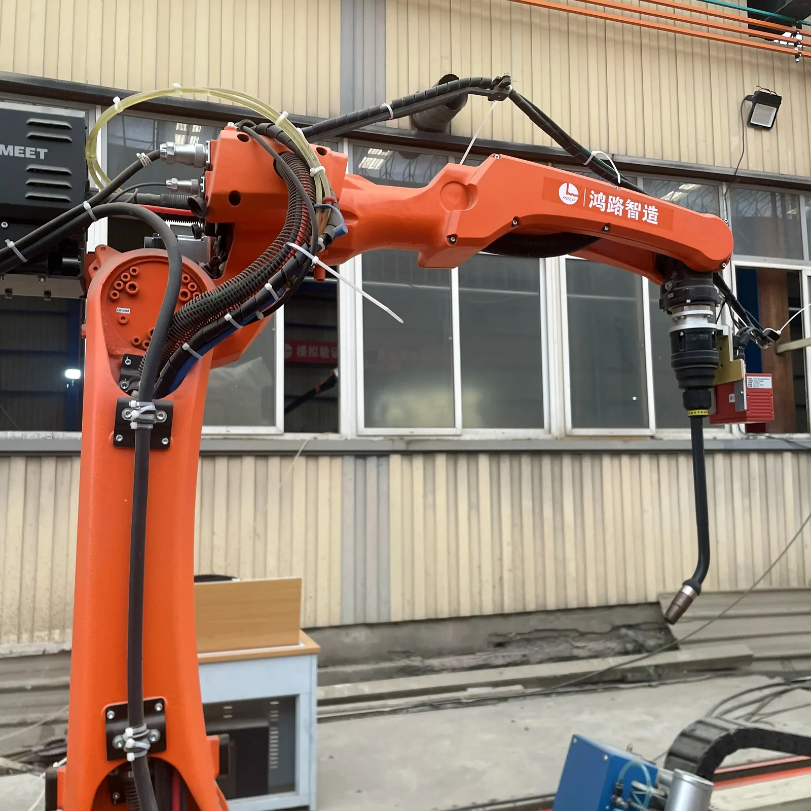 Close view of an orange welding robot arm, cabling and torch assembly in a factory