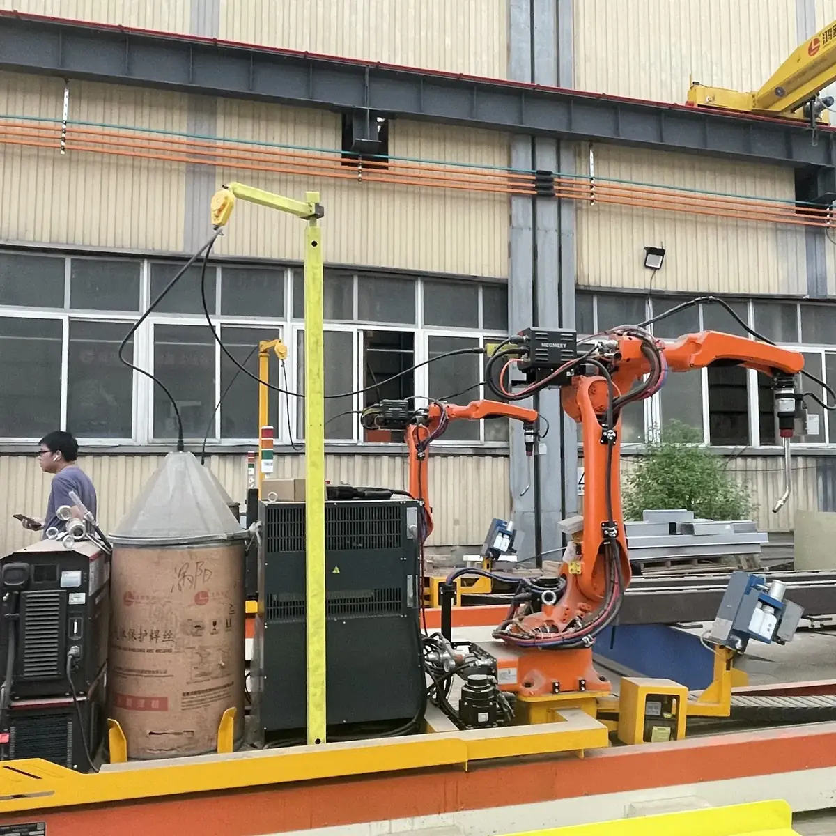 Rail-mounted welding station with power source and wire drum, with an operator nearby.