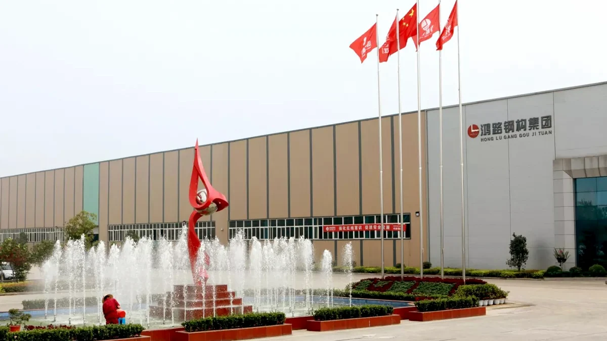 Exterior of our structural steel factory with flags, a fountain and the company name on the building.