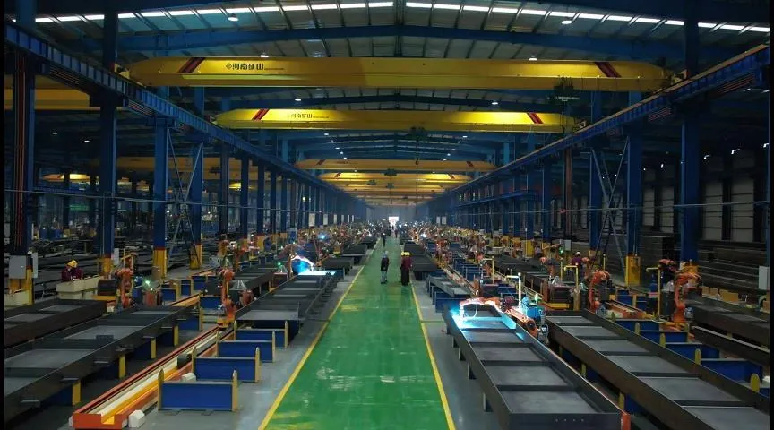 Central aisle of a welding robot hall with overhead cranes and steel members on both sides.